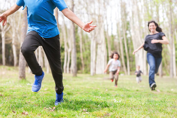 Group of children running with their mother through a meadow with trees.