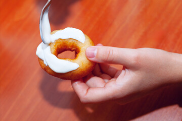 Hand holding a doughnut with cream on a wooden table, top view