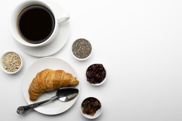 Breakfast with a cup of coffee. White cup with coffee close-up. Flatlay. Croissant on a plate with berries. Dried cranberries, raisins, chia seeds and peanuts are displayed nearby. Business break. 