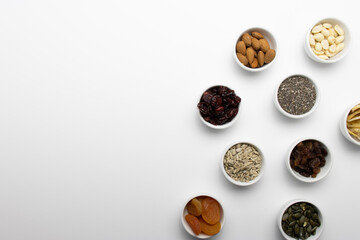Small ramekins stand on a white table. Ramekins contain peanuts, dried apricots, sunflower seeds, pumpkin seeds, dried cranberries, almonds, peanuts, chia seeds, dried bananas. Flatlay. close-up