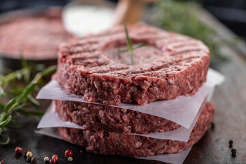 Fresh raw ground beef patties with rosemary salt and pepper made in a meat form on a cutting board - 789410624