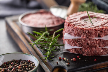 Fresh raw ground beef patties with rosemary salt and pepper made in a meat form on a cutting board - 789410662
