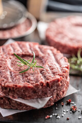 Fresh raw ground beef patties with rosemary salt and pepper made in a meat form on a cutting board