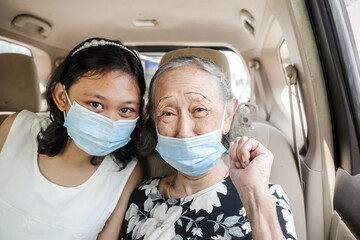 Asian teen girl and grandma wearing face masks inside a car