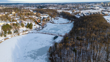 Drone photography of frozen lake, forest and city suburb landscape during winter day