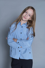 Confident young girl stands with arms crossed, wearing a smart blue shirt and black trousers, a blend of attitude and style.