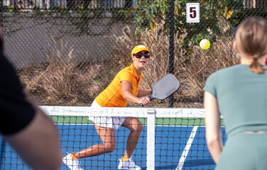 An active pickleball game happening on an outdoor court. The group of players are highly competitive in the popular sport. 