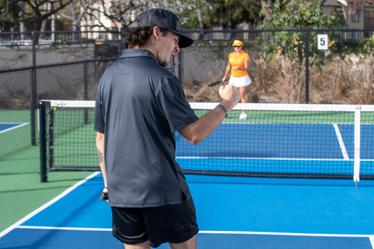 A man fist pumps after winning a pickleball game on an outdoor court. 