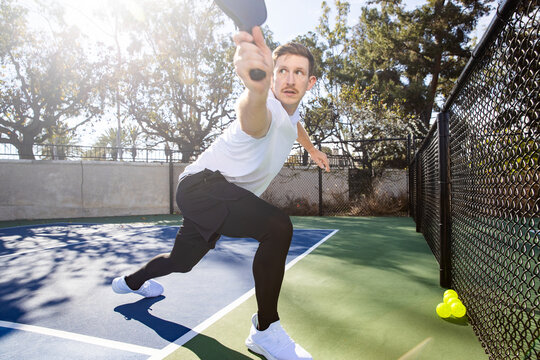 Pickleball player hitting the ball on court with his racquet. 