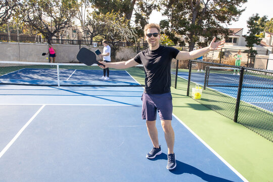 A confident man with his arms outstretched on a pickleball court. 