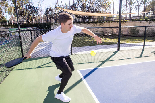 A man with a mustache returns a serve during a pickleball match on an outdoor court.