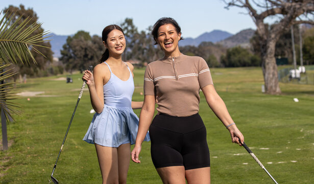 Two friends together on the golf course for a game. The female golfers are outside holding clubs and having fun