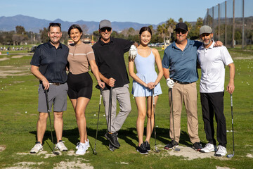 Group of golfers standing together outside on a golf course. The six friends are holding clubs on a sunny day, happy to play the game. 