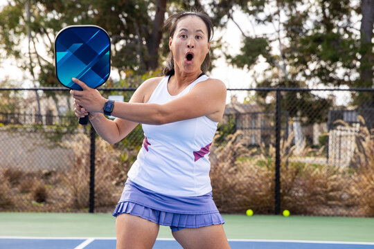 Female pickleball player having fun during a game on an outdoor court. She has a wild expression of shock and surprise.