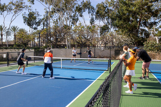 Pickleball players on an outdoor court playing the popular game. The sport is similar to tennis and allows for a diverse range of people to play. 