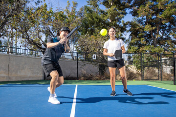 Co-Ed pickleball team playing a game together outside. The man and woman are athletic and working well as a team in the popular sport. 