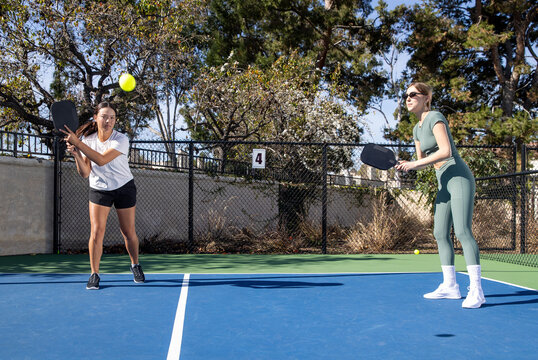 Two female pickleball players work together as a team during a game on an outdoor court. 