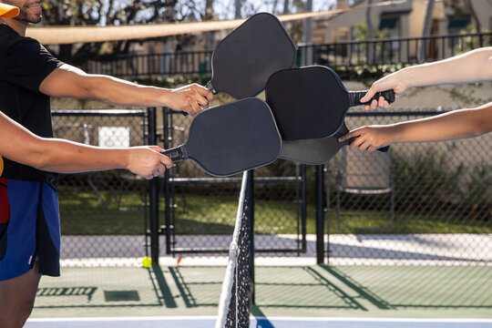 Four pickleball players tapping racquets over the net after a fun game in the sun outside. 