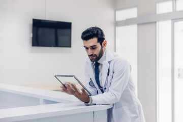 Doctor Wearing Scrubs In Hospital Corridor Using Digital Tablet. Doctor holding digital tablet....