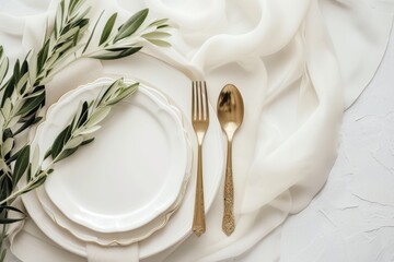 Elegant table setting with white plates, gold cutlery, and olive branch.