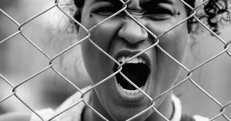 Desperate Young African American woman feeling outrage screaming with rage behind metal fence...