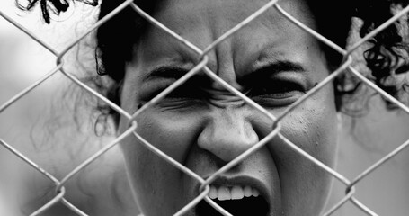 Desperate Young African American woman feeling outrage screaming with rage behind metal fence...