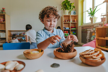 Boy playing in kindergarten with natural toys, seashells, pine cones, feathers