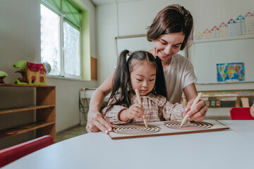Girl and teacher playing with educational wooden toys developing coordination with tabletop labyrinths in a kindergarten