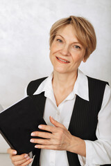 Portrait of business woman. Confident, successful mature woman holding black diary on light gray background. Looking at camera. High quality photo