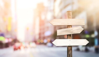 Wooden signpost with blank white arrows pointing in different directions against a blurred city background