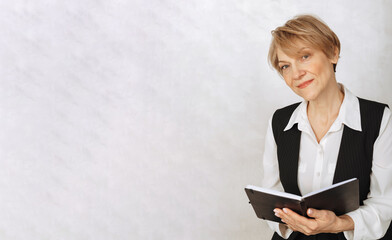 Portrait of business woman. Confident, successful mature woman holding black diary on light gray background. Looking at camera, banner. High quality photo