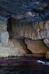 ZURRIEQ, MALTA - Augusts 06, 2021: The Blue Grotto - A famous sea cave surrounded by the deep blue sea at southern Malta. On a traditional boat surrounded by more brightly coloured boats. 