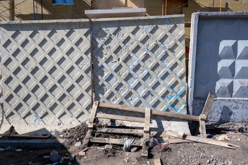 A rickety monolithic concrete fence at a construction site with debris on the ground