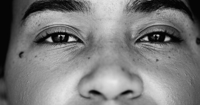 Intense macro close-up face of one young black woman facial eyesight features in monochrome, black and white gaze at camera