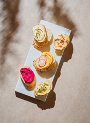 Diverse healthy hummus crostini appetizers with different types of hummus: carrot, beetroot, classic on a marbre board. Vegan food. Still Life, harsh lighting, shadows, top view, copy space.