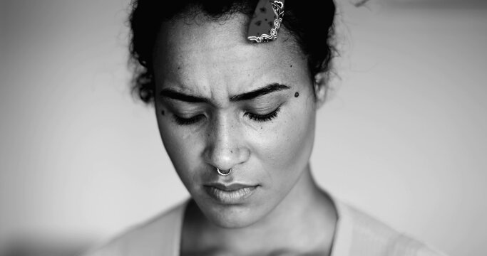 One anxious young black woman close-up face expressing preoccupation and mental despair in dramatic black and white. Desperate 20s person of African descent