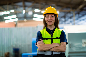 A woman wearing a yellow helmet and a safety vest is smiling for the camera. She is standing in a...