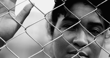 One Confined young black woman leaning on metal fence closing and opening eyes while hand holds on...