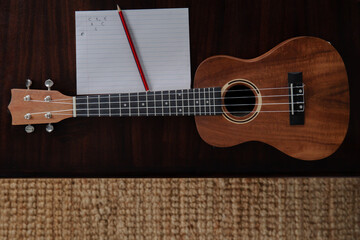 Ukulele, pencil and paper. Writing a song. Ukulele on a wooden table