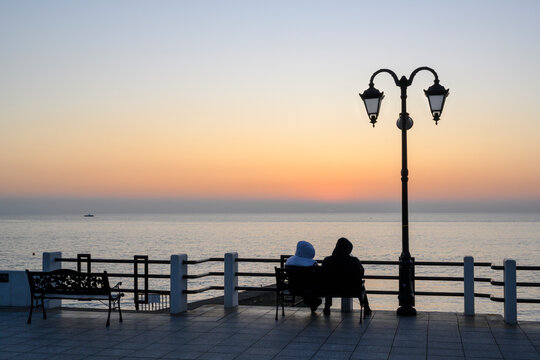 Silhouette of a couple on the sea embankment with a pier and a lantern at sunset