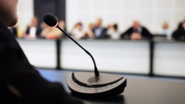 Debate or political campaign speech of female speaker talking confidently about strategy in microphone sitting at round table in conference room. Adult business woman discusses partnership