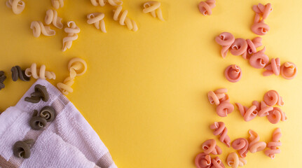 Fototapeta na wymiar Brown pink and green insalatonde pasta on a yellow background. There is a white towel next to the pasta. Place for text in the center of the image. negative space. Raw pasta. Close-up. Flatlay
