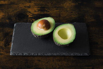Two avocados halved on a rectangular slate cutting board, ready to be used as an ingredient in...