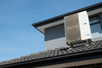 Air conditioning system on the tiled roof of a private house against a blue sky. Cooling in the summer and alternative energy for heating due to inflation and high energy costs
