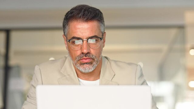 Middle aged busy business man trader broker analyst investor analyzing stock exchange trade crypto financial market looking at computer screen wearing glasses with digital chart reflection.