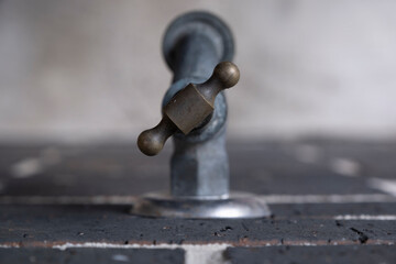 Water tap on a black brick wall, seen from above. Focus on the brass handle. Narrow depth of field
