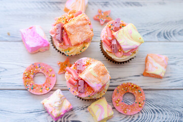 Pastel colored pink cupcakes with chocolate, donuts and rainbow marshmallow