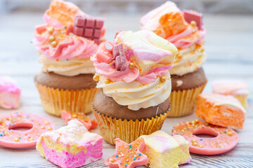 Pastel colored pink cupcakes with chocolate, donuts and rainbow marshmallow