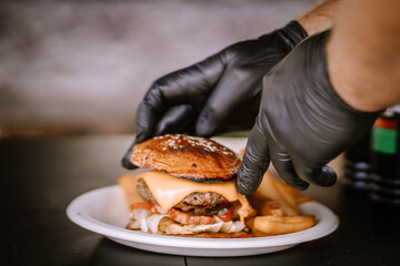 Valmiera, Latvia- July 29, 2023 - A close-up of gloved hands placing a sesame bun on top of a...