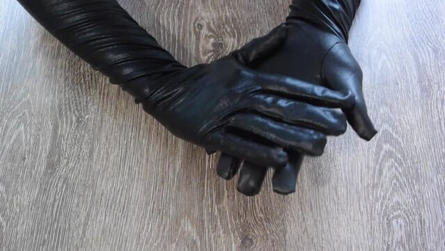 Horizontal Full HD video. Top view. Female hands in black leather latex gloves rub their palms on wooden table. Woman snaps her fingers. Concept of adult game, festival, masquerade